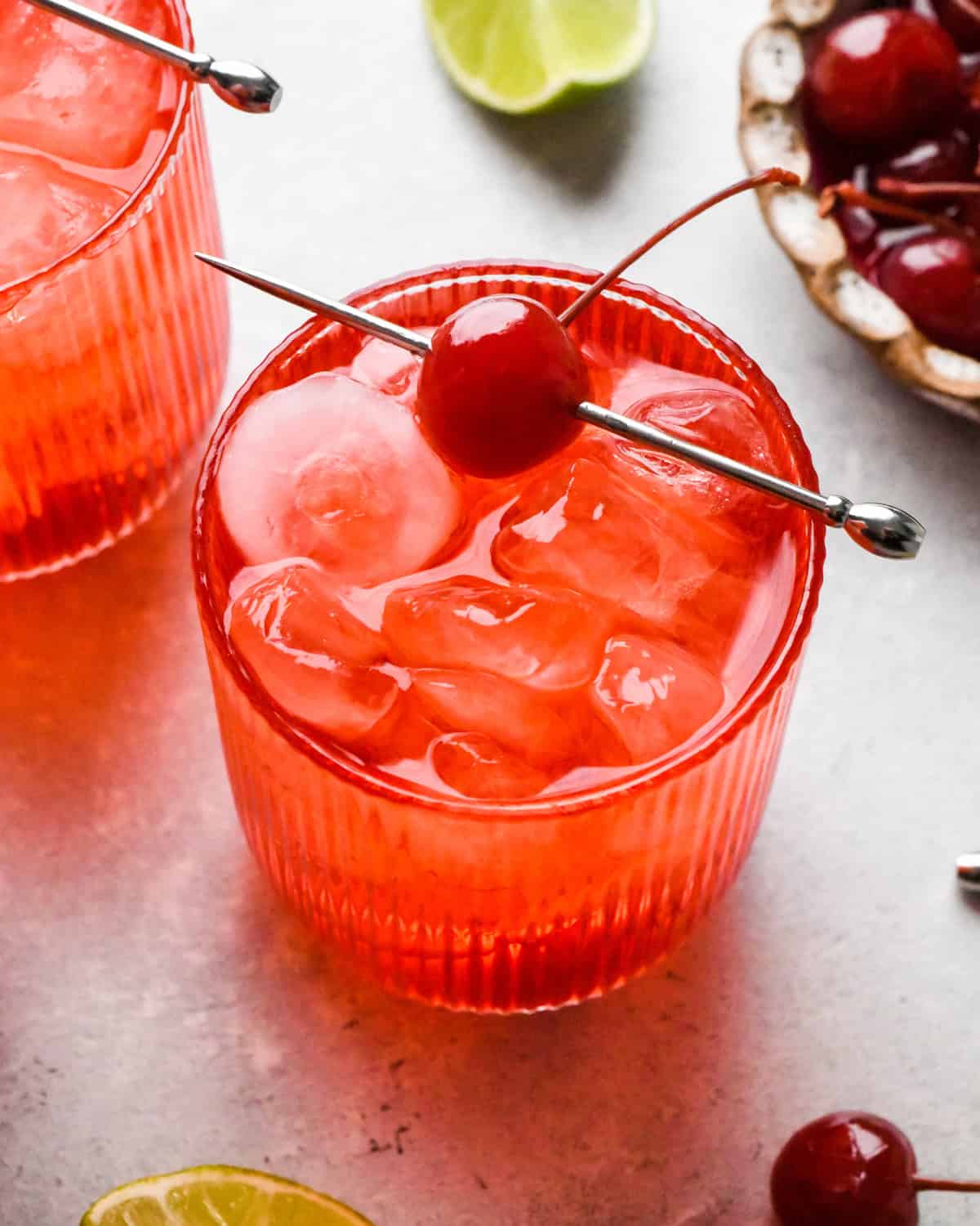 Close-up photo of a Shirley Temple served over ice in a glass, garnished with a maraschino cherry on a cocktail pick.