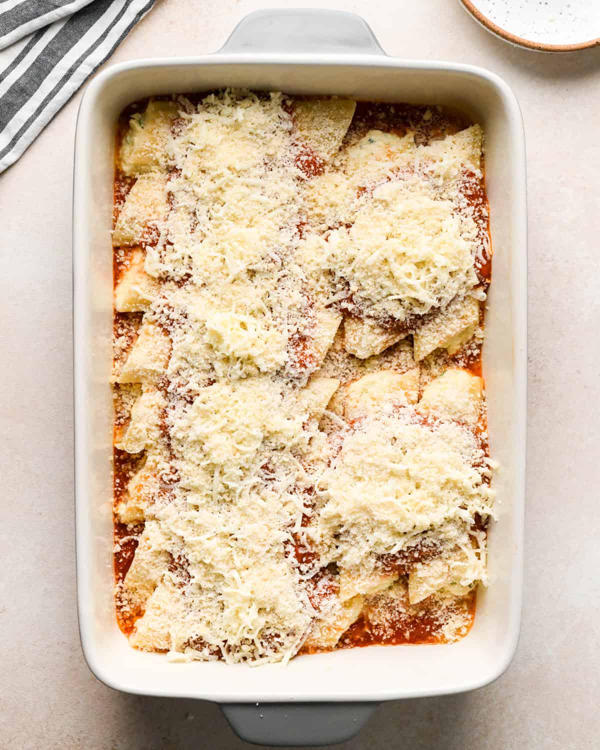 Making stuffed manicotti - overhead photo of stuffed manicotti noodles in a casserole dish topped with marinara sauce, parmesan cheese, and mozzarella cheese.