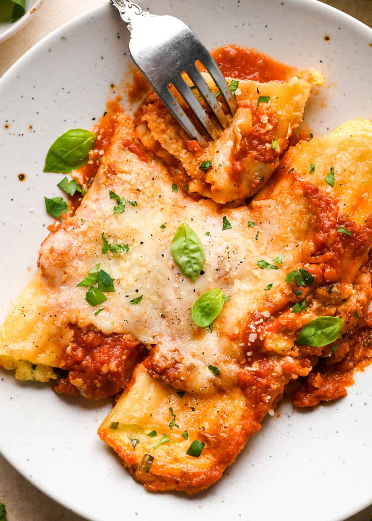 Close-up view of stuffed manicotti topped with fresh basil and cracked pepper, being served on a white speckled plate with a fork.