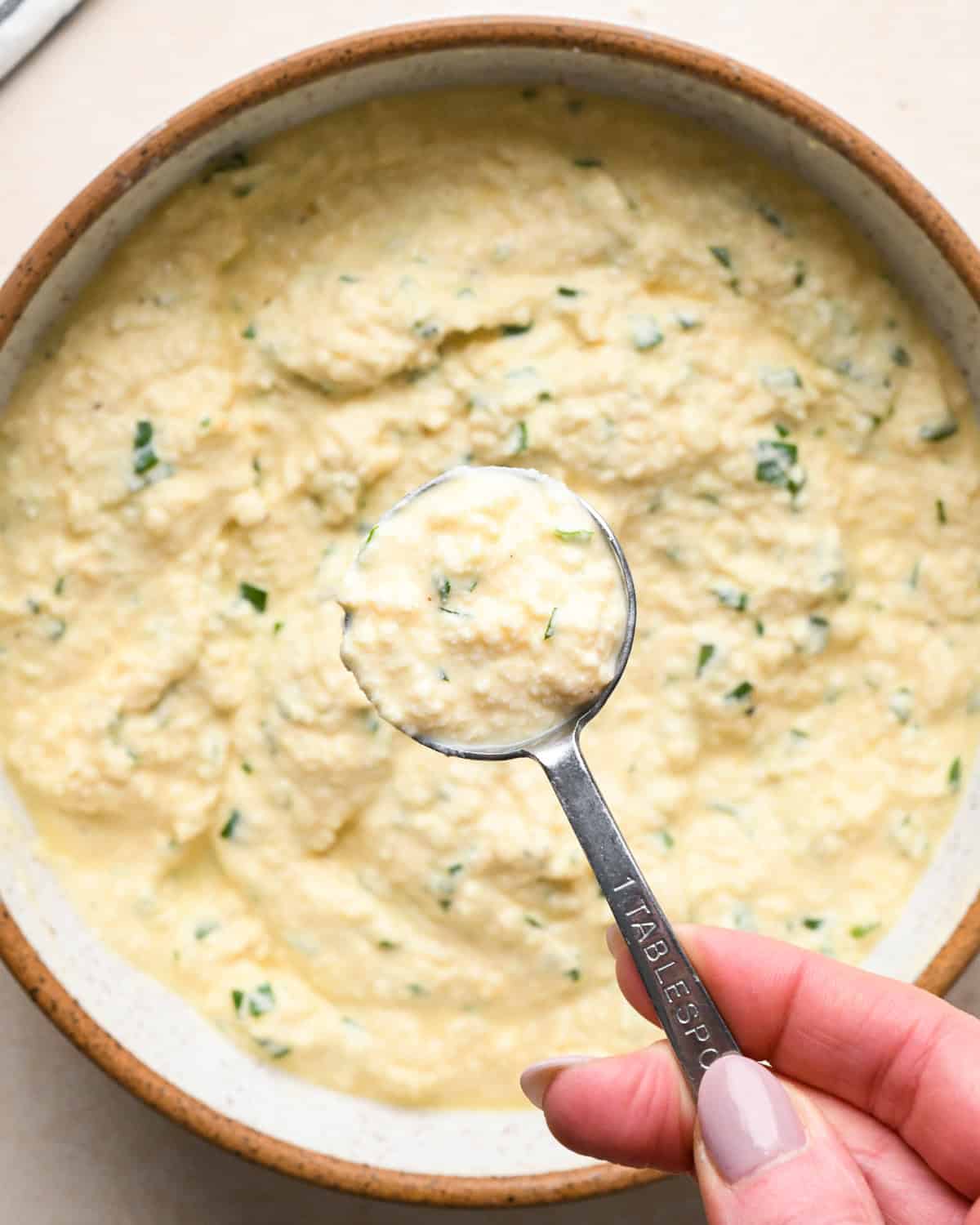 Making stuffed manicotti - overhead photo of manicotti filling being scooped out of a bowl with a measuring tablespoon.