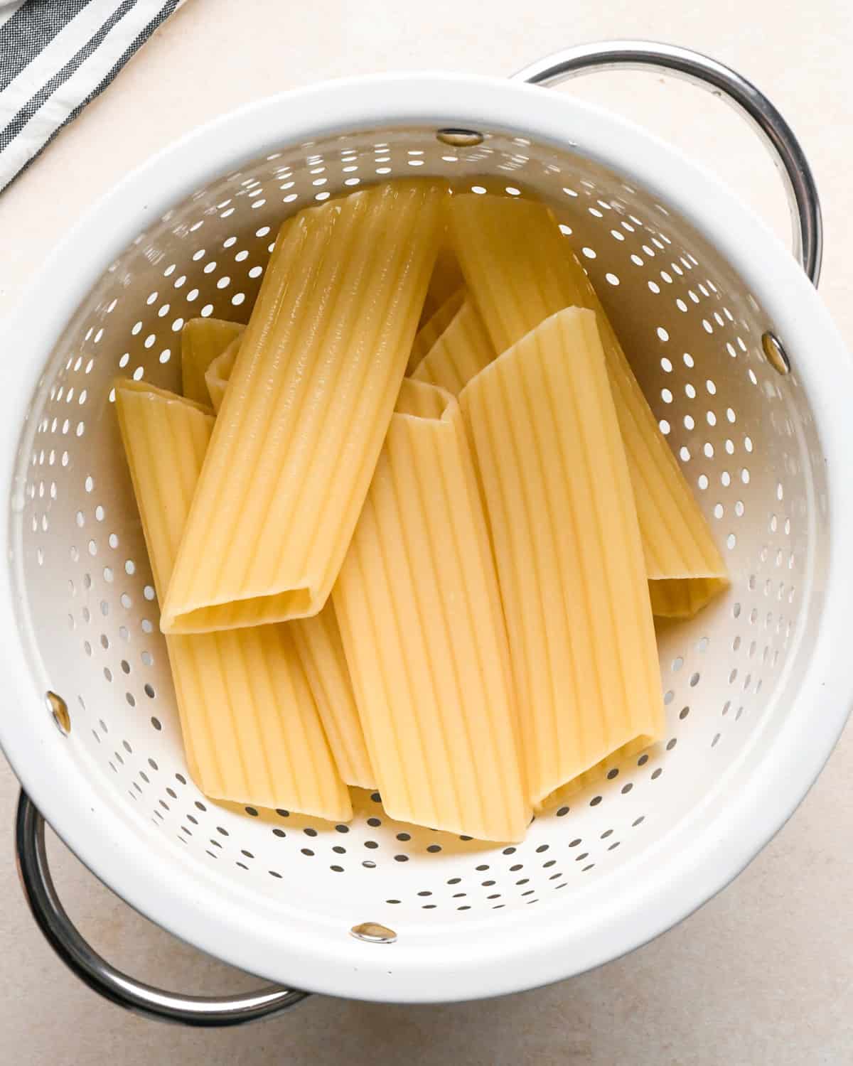 Making stuffed manicotti - overhead photo of cooked manicotti noodles being strained in a white colander.
