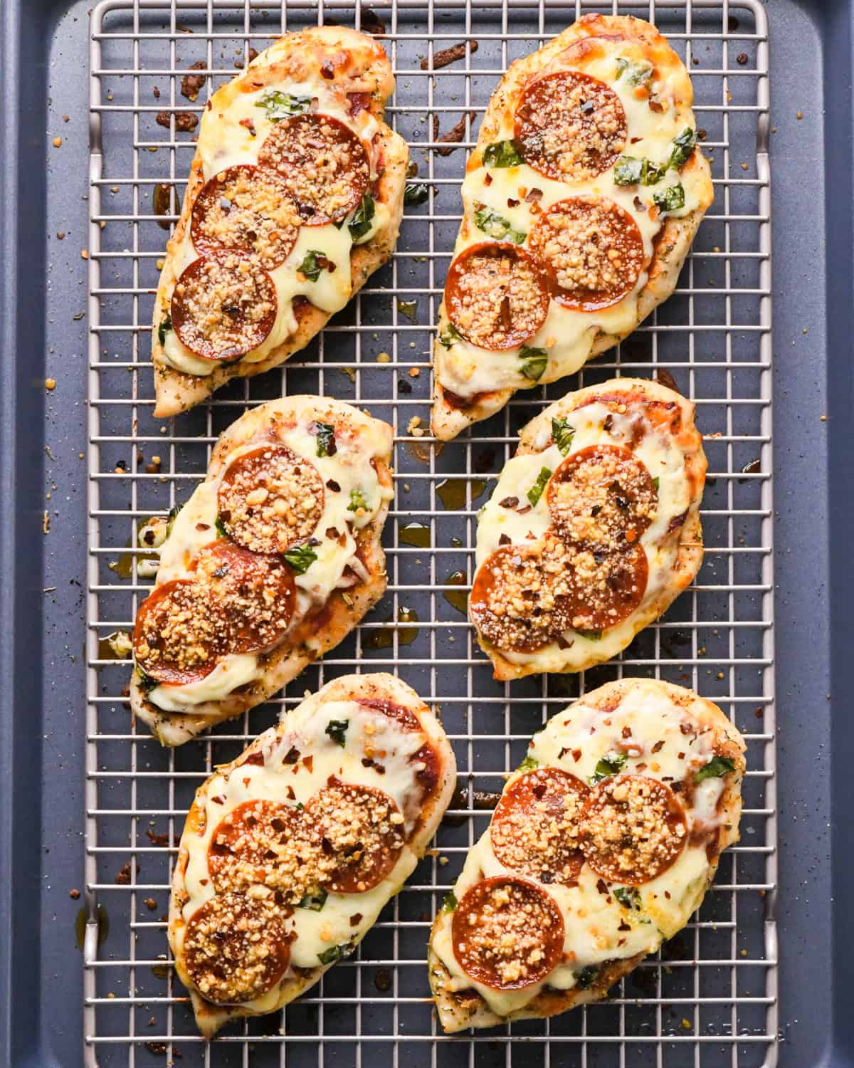 Making pizza chicken: overhead photo of chicken breasts topped with spices, pizza sauce, mozzarella cheese, and fresh basil leaves after baking in the oven.