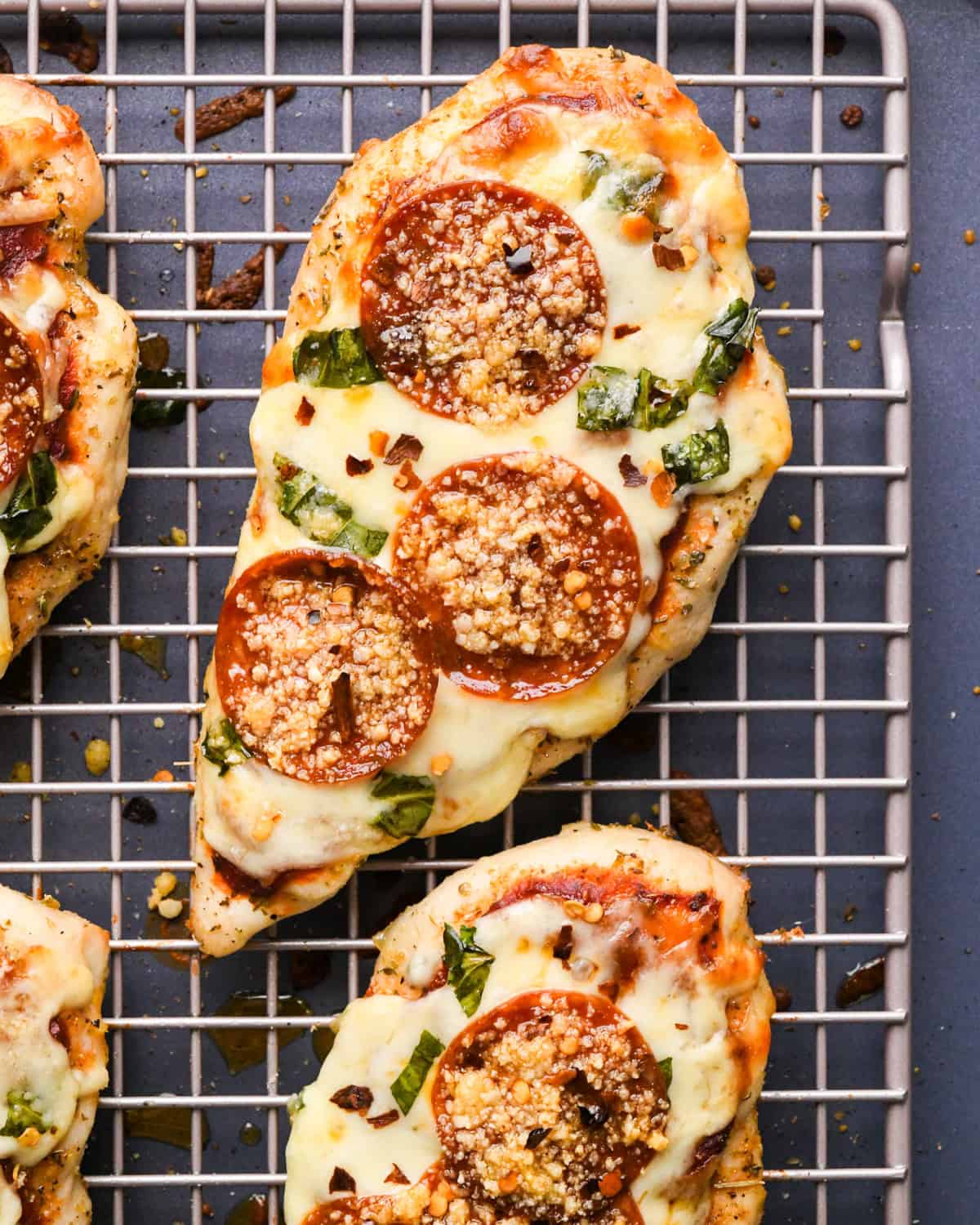 Making pizza chicken: close-up photo of chicken breasts topped with spices, pizza sauce, mozzarella cheese, and fresh basil leaves after baking in the oven.