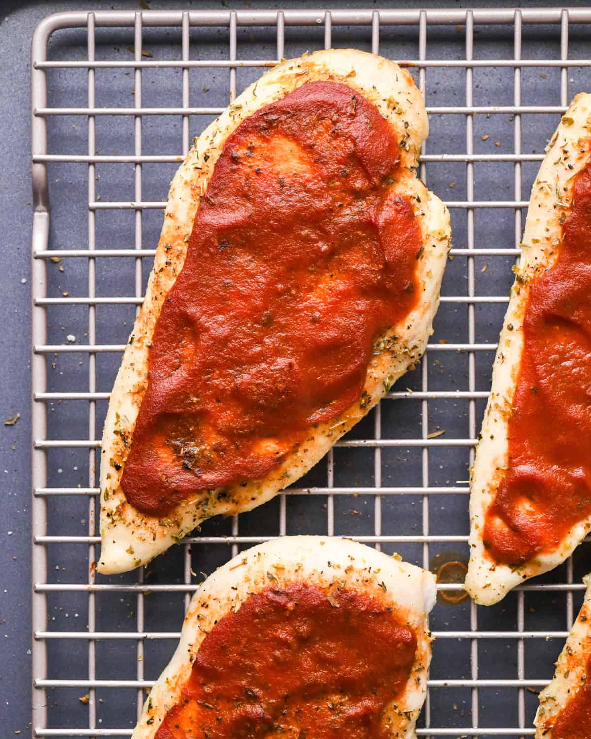 Making pizza chicken: close-up photo of chicken breasts sprinkled with spices and topped with pizza sauce.