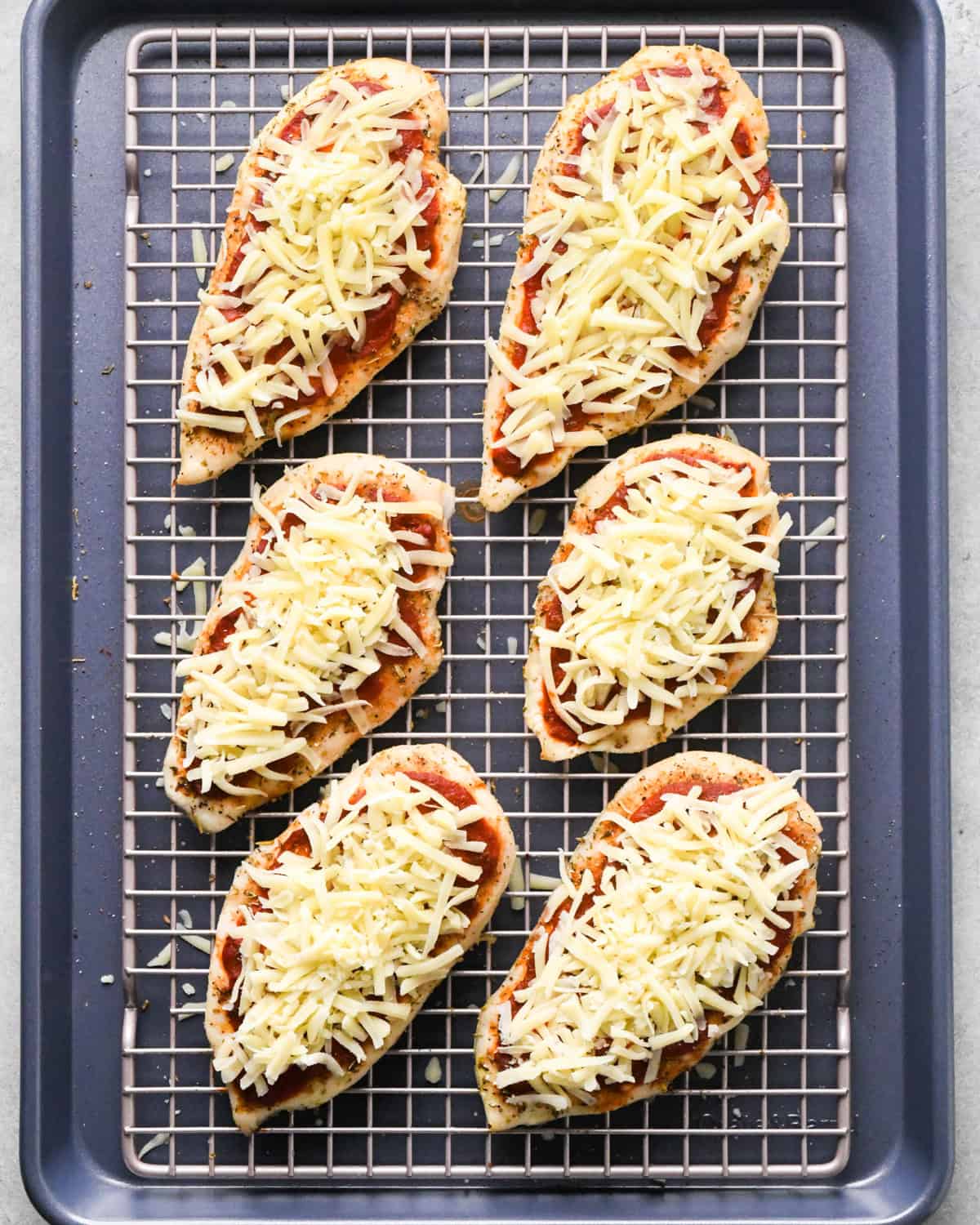 Making pizza chicken: overhead photo of chicken breasts topped with spices, pizza sauce, and mozzarella cheese.