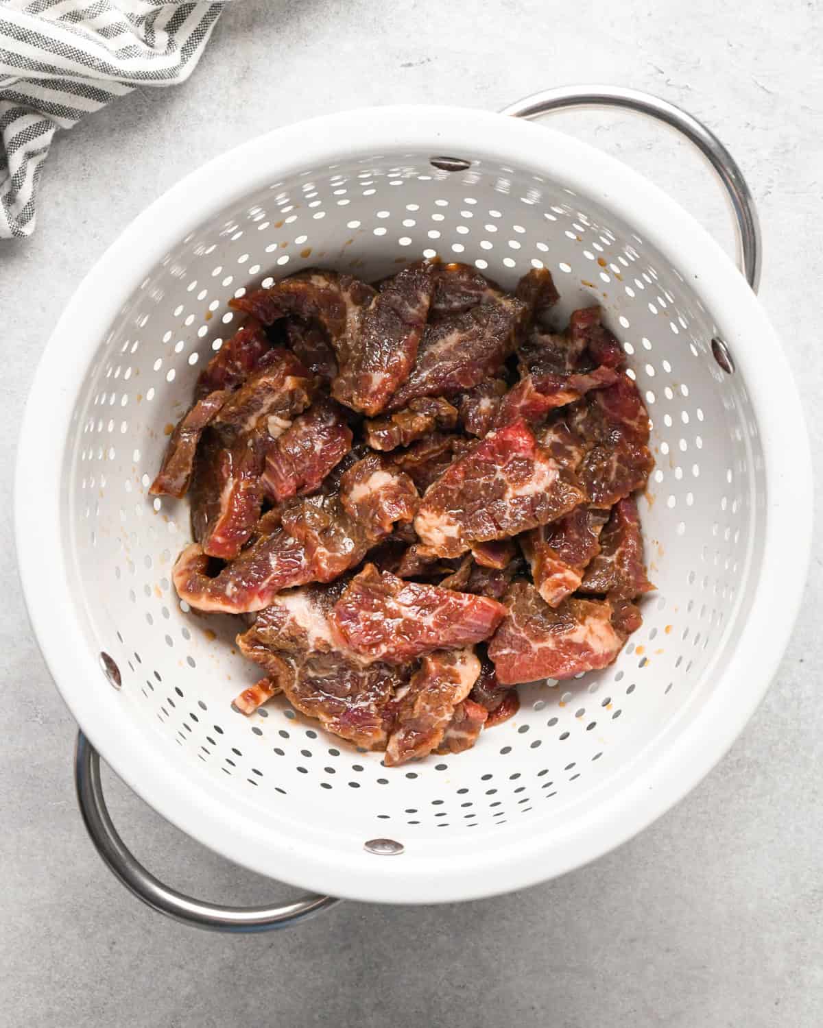 Making beef and broccoli: overview photo of marinated flank steak placed in a colander to drain extra liquid.