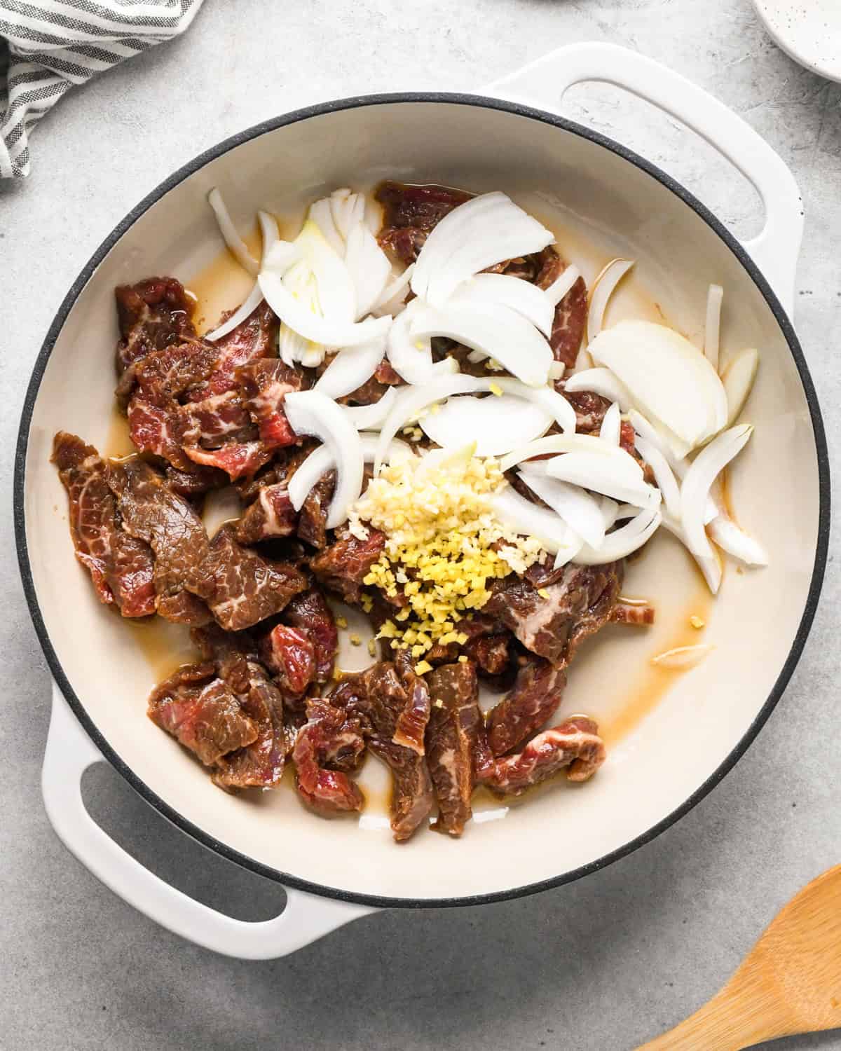 Making beef and broccoli: flank steak, onions, and spices are added to a white pan to be sautéed.