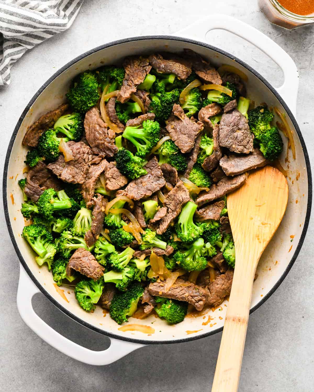 Making beef and broccoli: overview photo of completed stir-fry, in a white pan, being stirred with a wooden spatula.