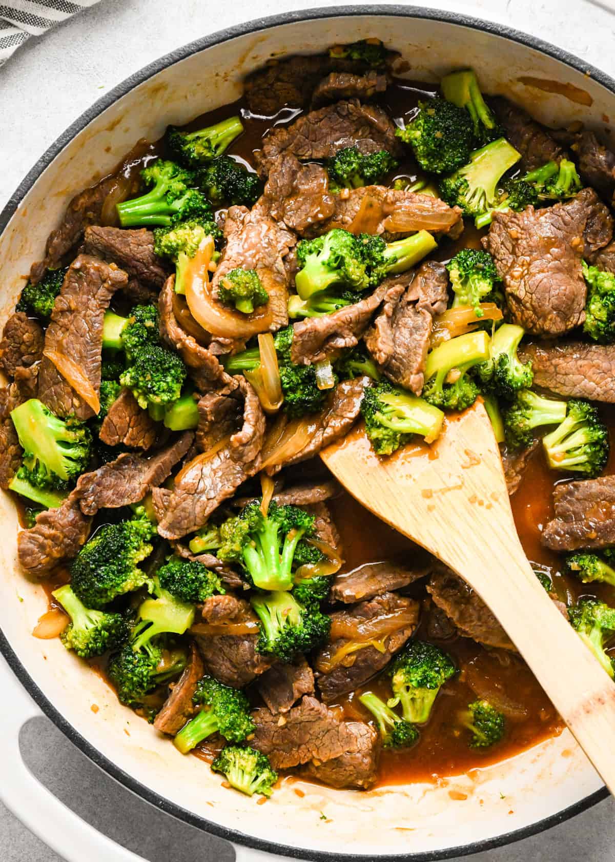 Making beef and broccoli: overview photo of beef and broccoli stir-fry ready to be served and being stirred with a wooden spatula.
