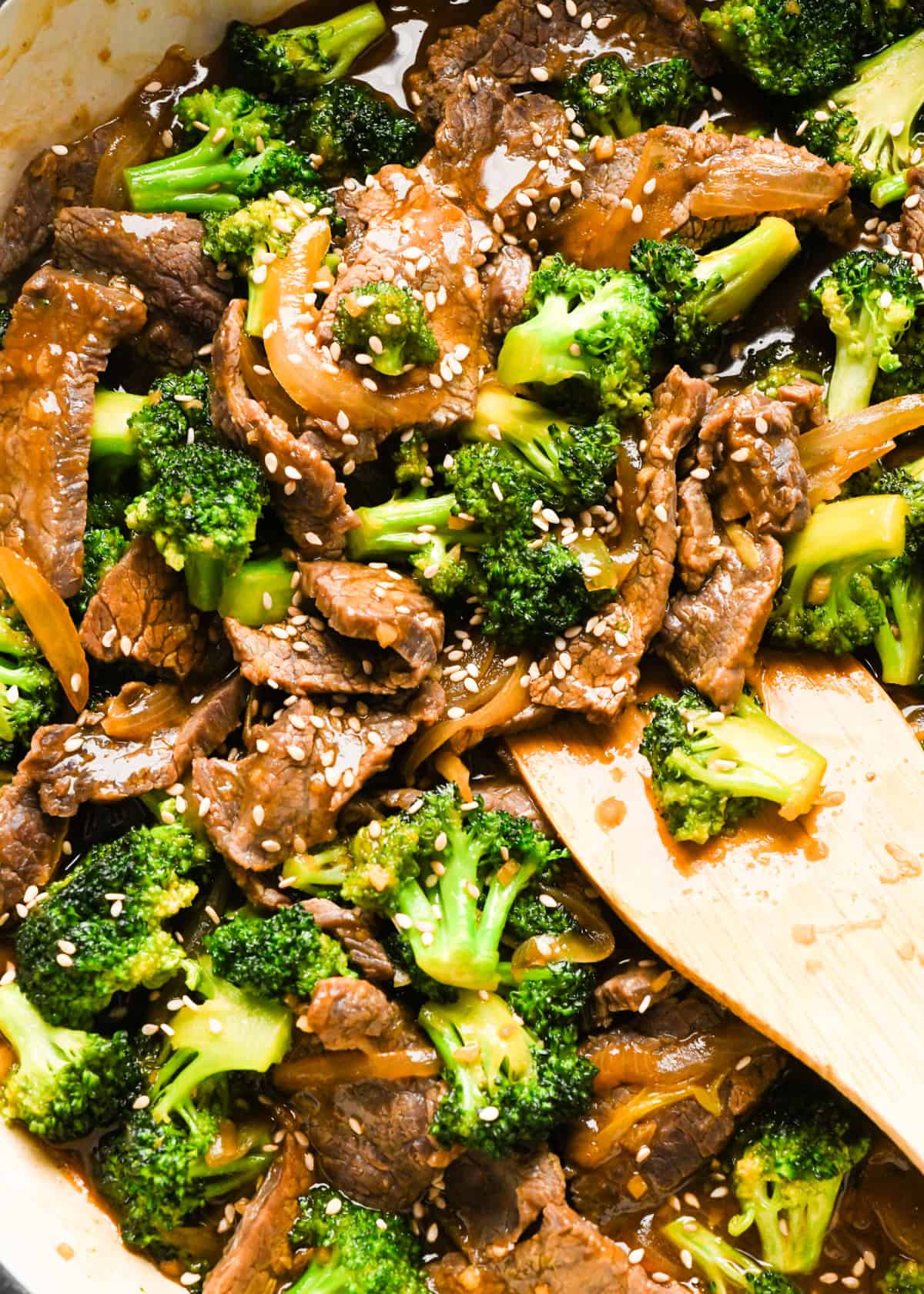 Making beef and broccoli: overview photo of stir-fry topped with sesame seeds and being stirred with a wooden spatula.