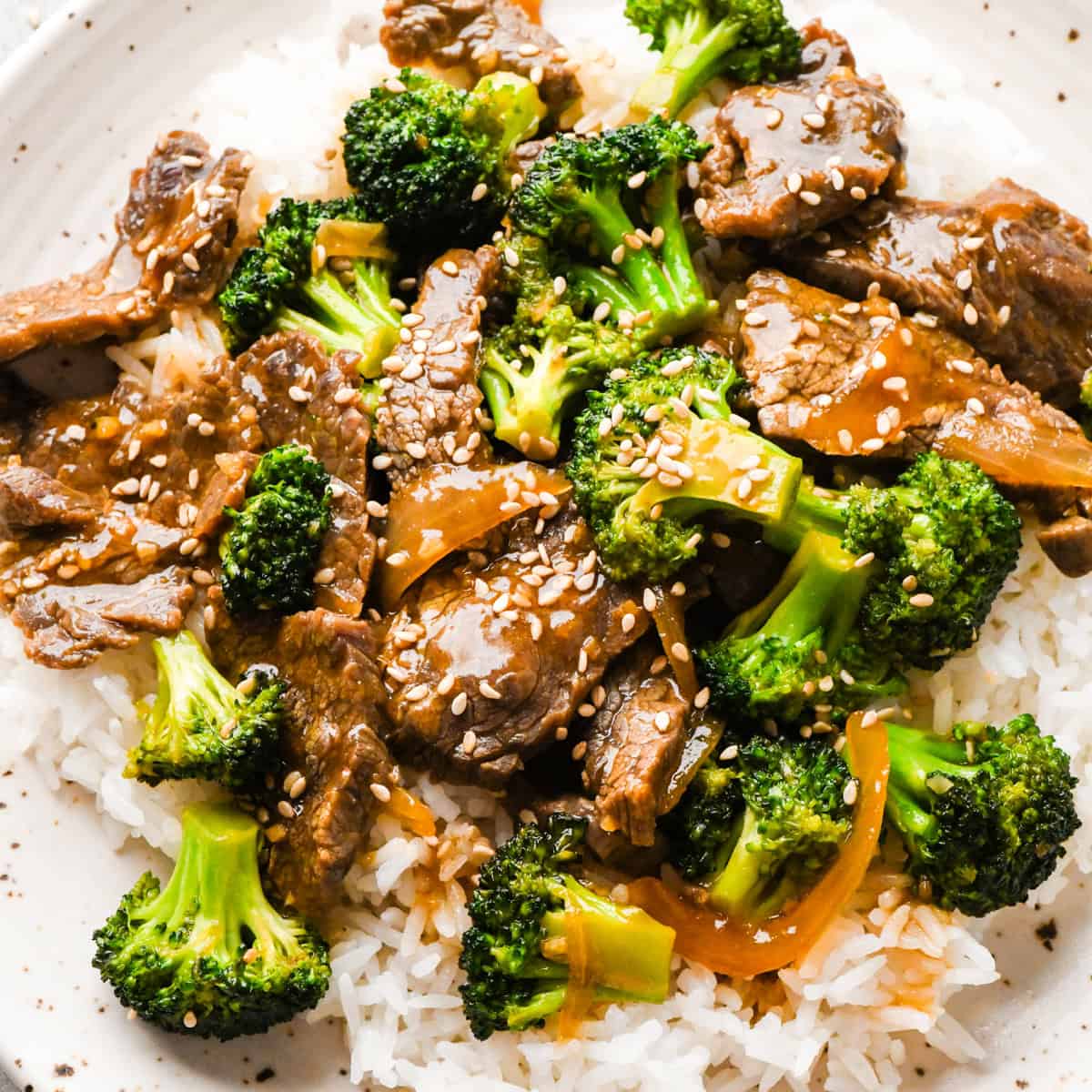 Overview photo of beef and broccoli stir-fry served over white rice with sesame seeds on top.