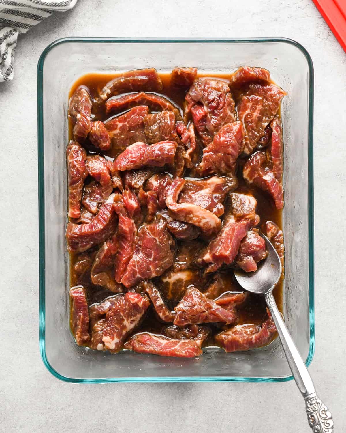 Making beef and broccoli: overview photo of a clear rectangle serving dish with marinated flank steak.