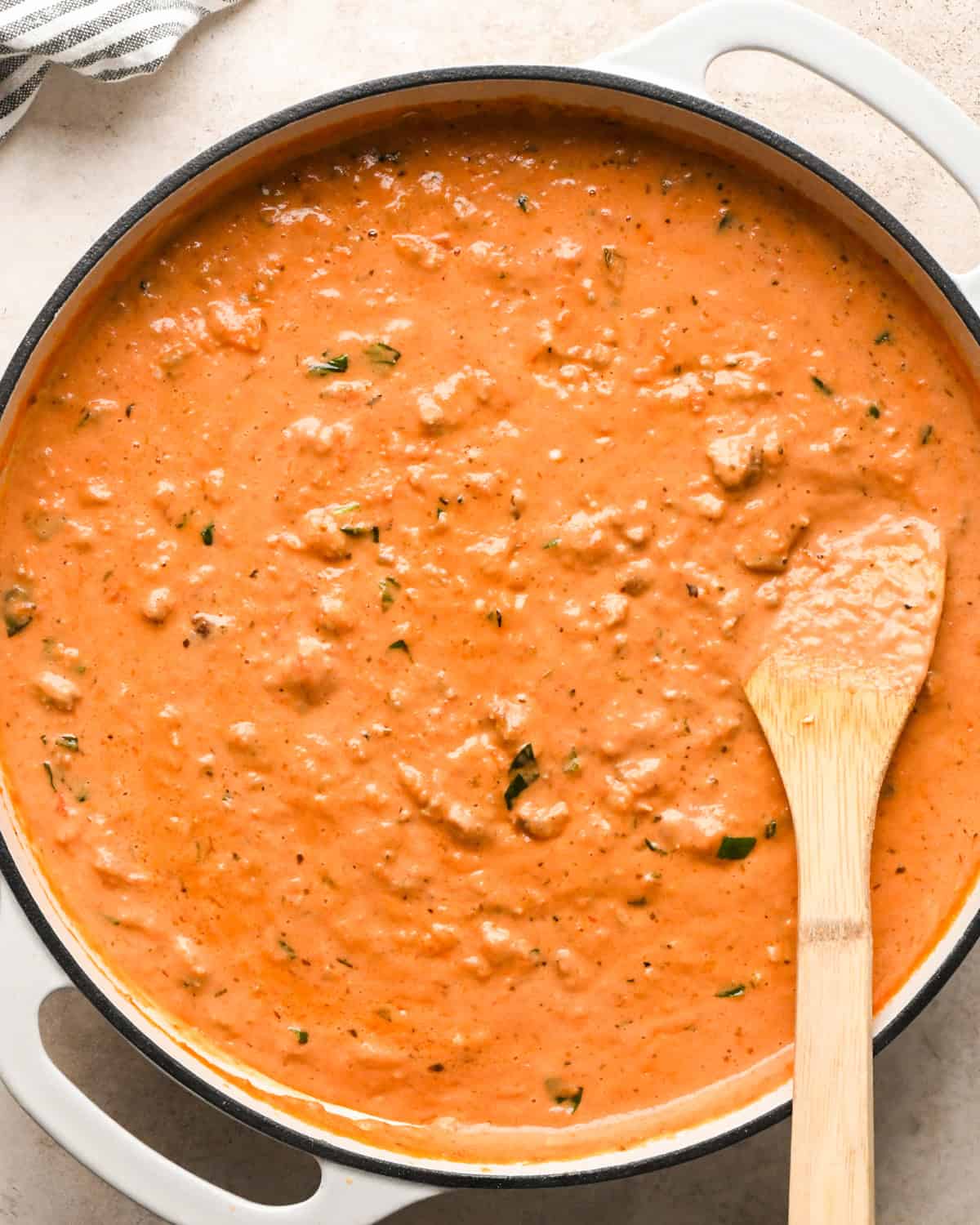 Making sausage pasta: overhead photo of completed meat sauce in a white skillet being stirred with a wooden spoon.