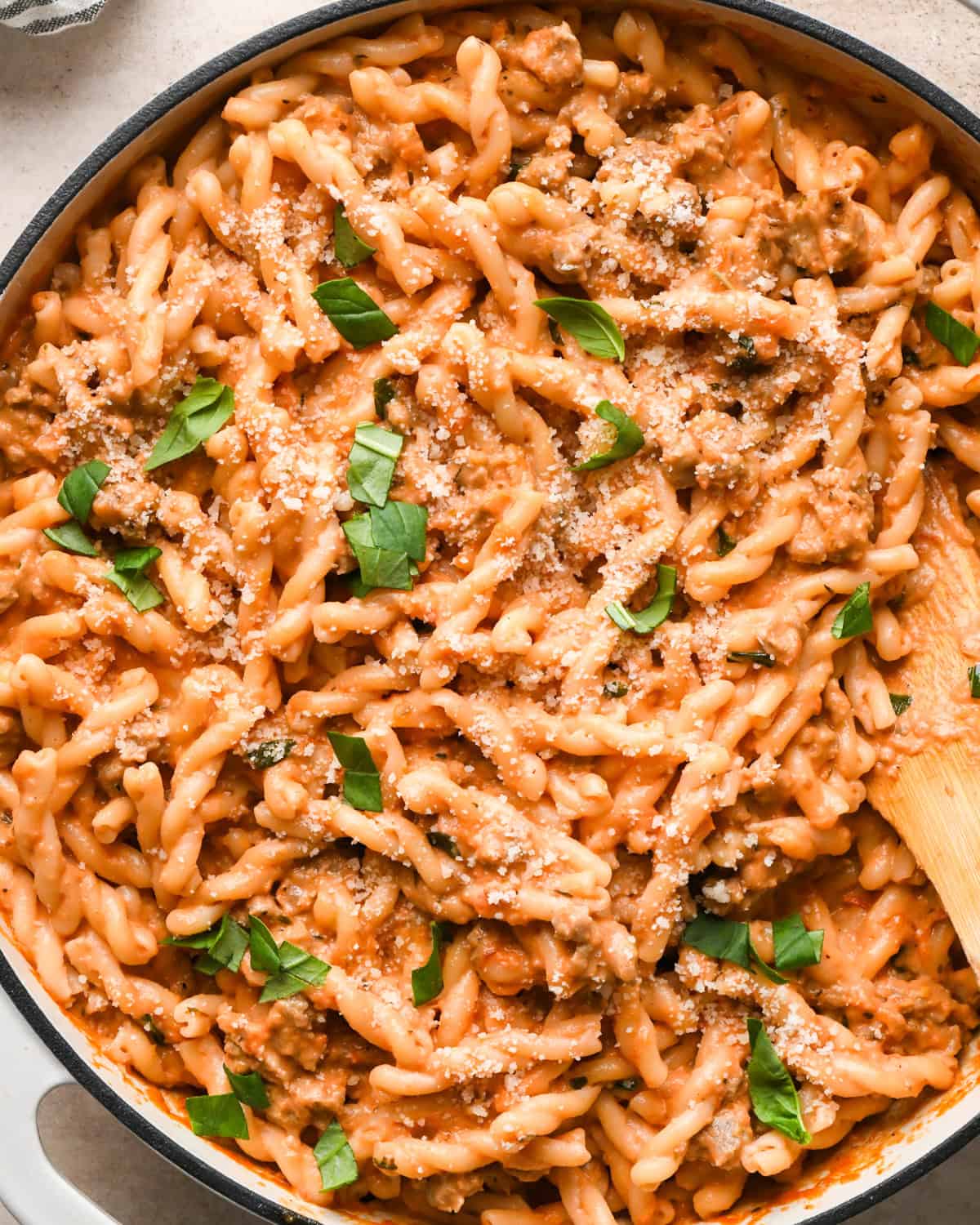 A pot of creamy sausage pasta topped with grated Parmesan cheese and fresh basil leaves.