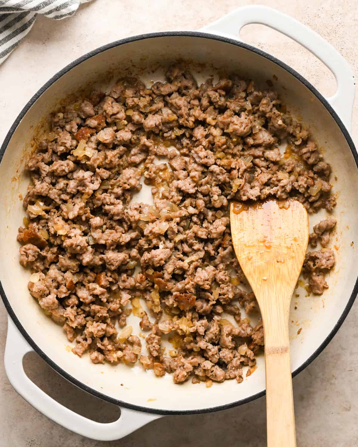 Making sausage pasta: overhead photo of Italian sausage, garlic, and onion cooked in a white skillet and being stirred with a wooden spatula.