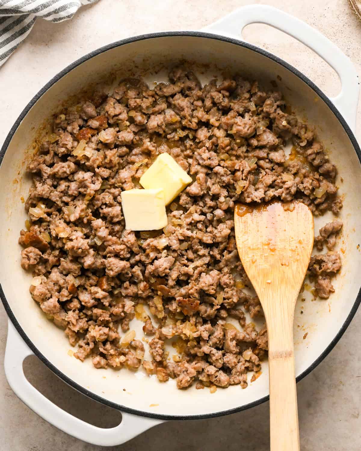 Making sausage pasta: overhead photo of Italian sausage, garlic, and onion cooked in a white skillet and being stirred with a wooden spatula. Butter has just been added.