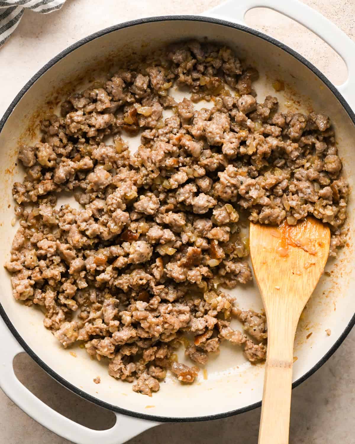 Making sausage pasta: overhead photo of Italian sausage, garlic, butter, flour, and onion cooked in a white skillet and being stirred with a wooden spatula.