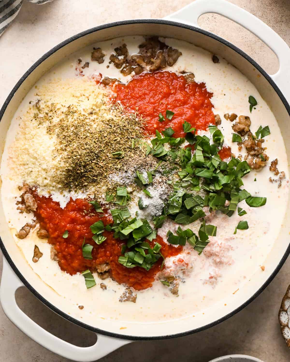 Making sausage pasta: overhead photo of pasta sauce ingredients being added to a white skillet.