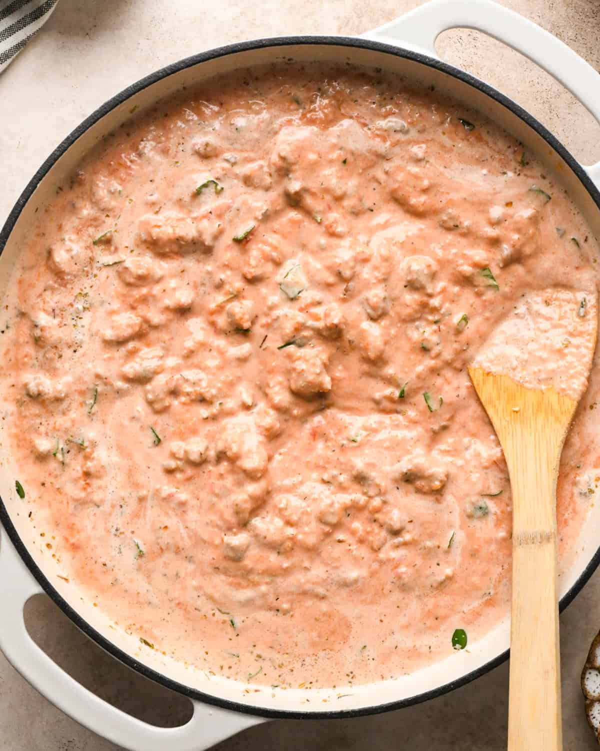 Making sausage pasta: overhead photo of completed meat sauce in a white skillet being stirred with a wooden spoon.