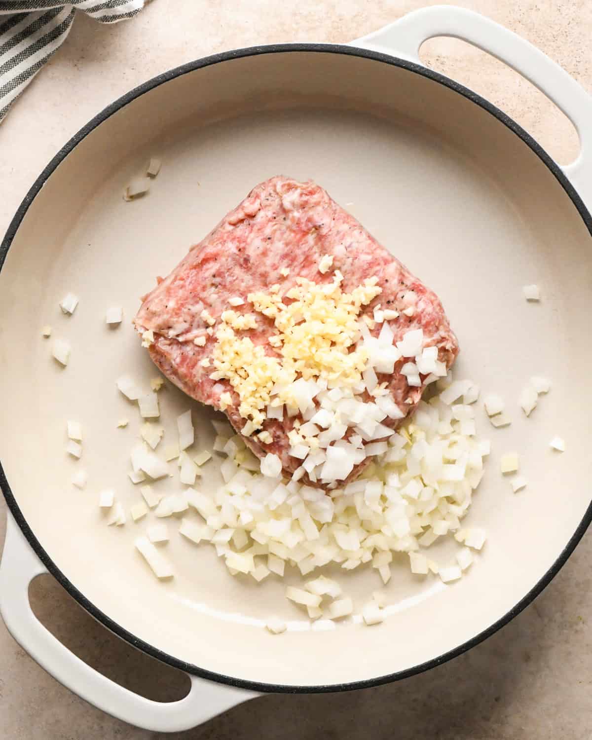 Making sausage pasta: overhead photo of Italian sausage, garlic, and onion being cooked in a white skillet.
