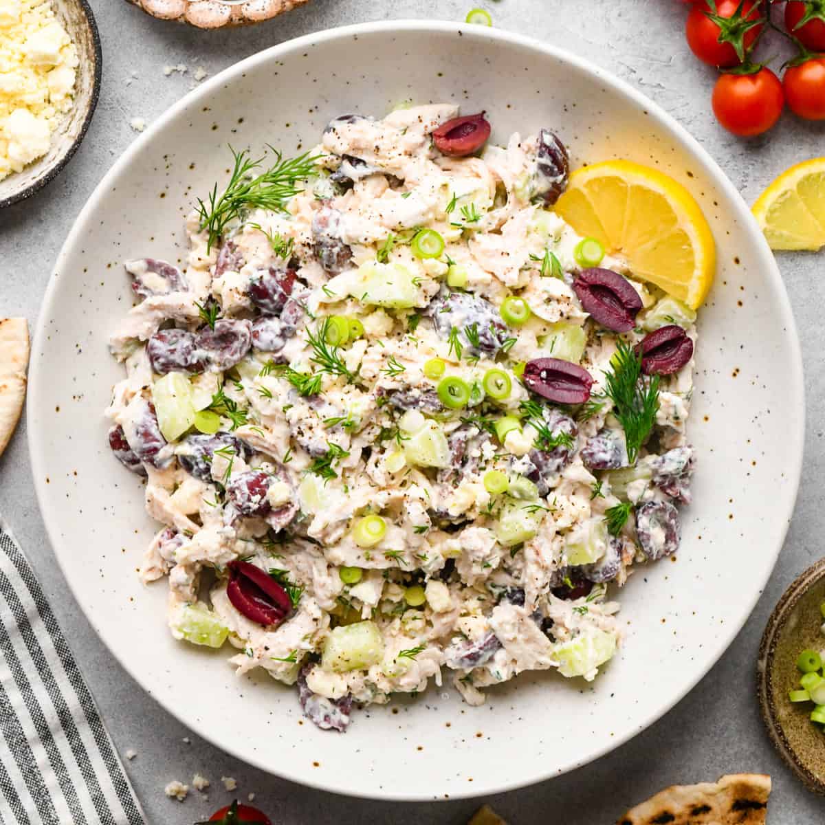 Overview photo of Greek chicken salad being served in a white speckled bowl with a slice of lemon.