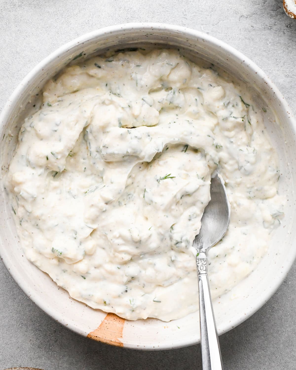 Making Greek chicken salad: the finalized dressing is shown in a white speckled bowl with a spoon.