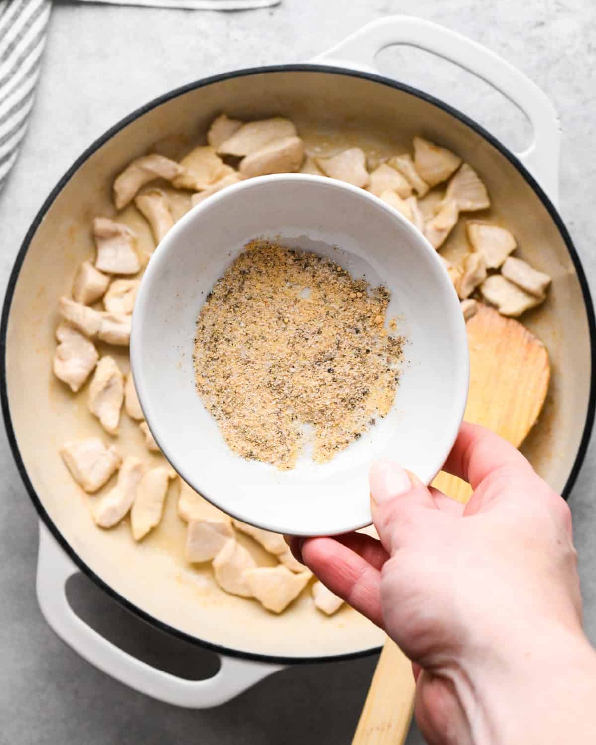 Making chicken fried rice: overhead photo of spices being added to a white skillet with cooked chicken.