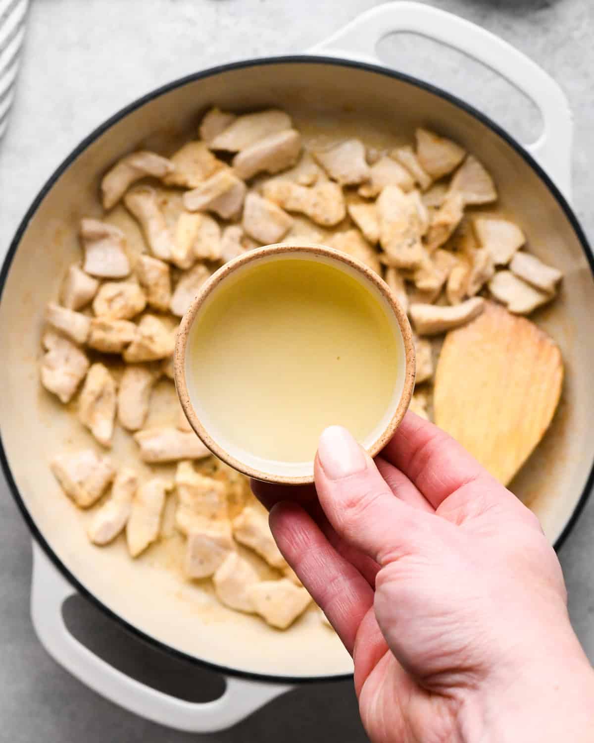 Making chicken fried rice: overhead photo of sauce being added to a white skillet with cooked chicken and spices.