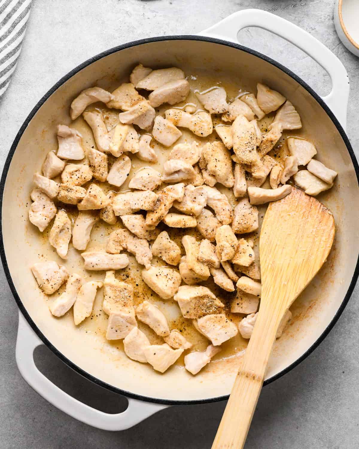 Making chicken fried rice: overhead photo of chicken, spices, and sauce being stirred together with a wooden spatula in a white skillet.