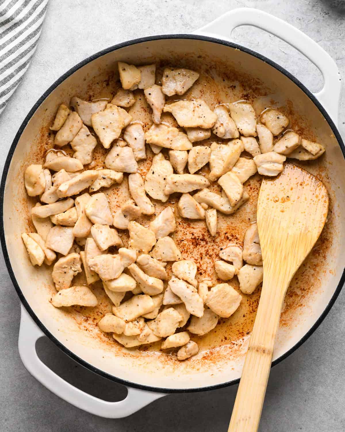 Making chicken fried rice: overhead photo of chicken, spices, and sauce being stirred together with a wooden spatula in a white skillet.