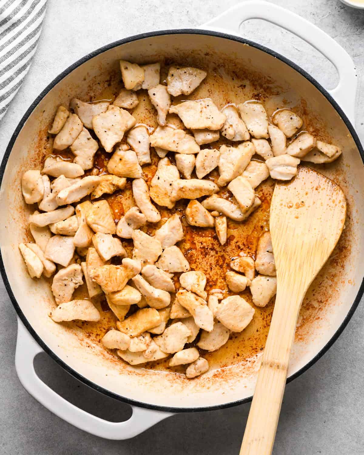 Making chicken fried rice: overhead photo of chicken, spices, and sauce being stirred together with a wooden spatula in a white skillet.