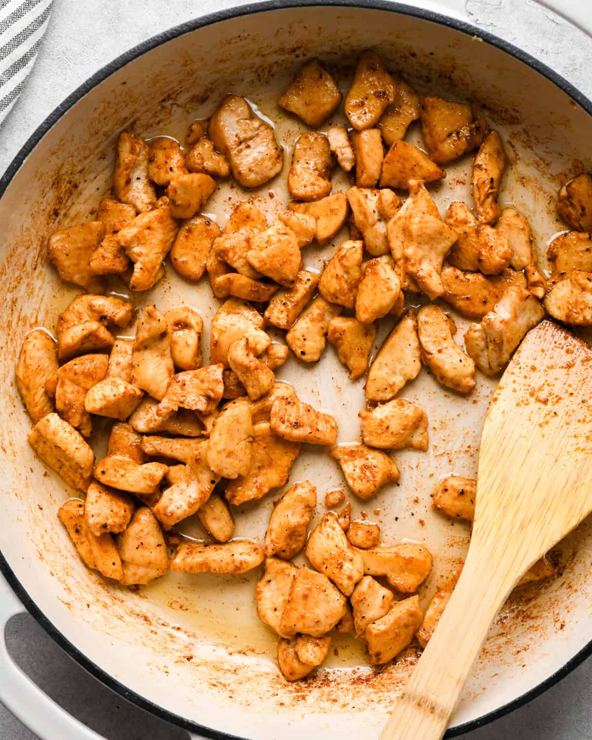 Making chicken fried rice: overhead photo of chicken, spices, and sauce being stirred together with a wooden spatula in a white skillet.