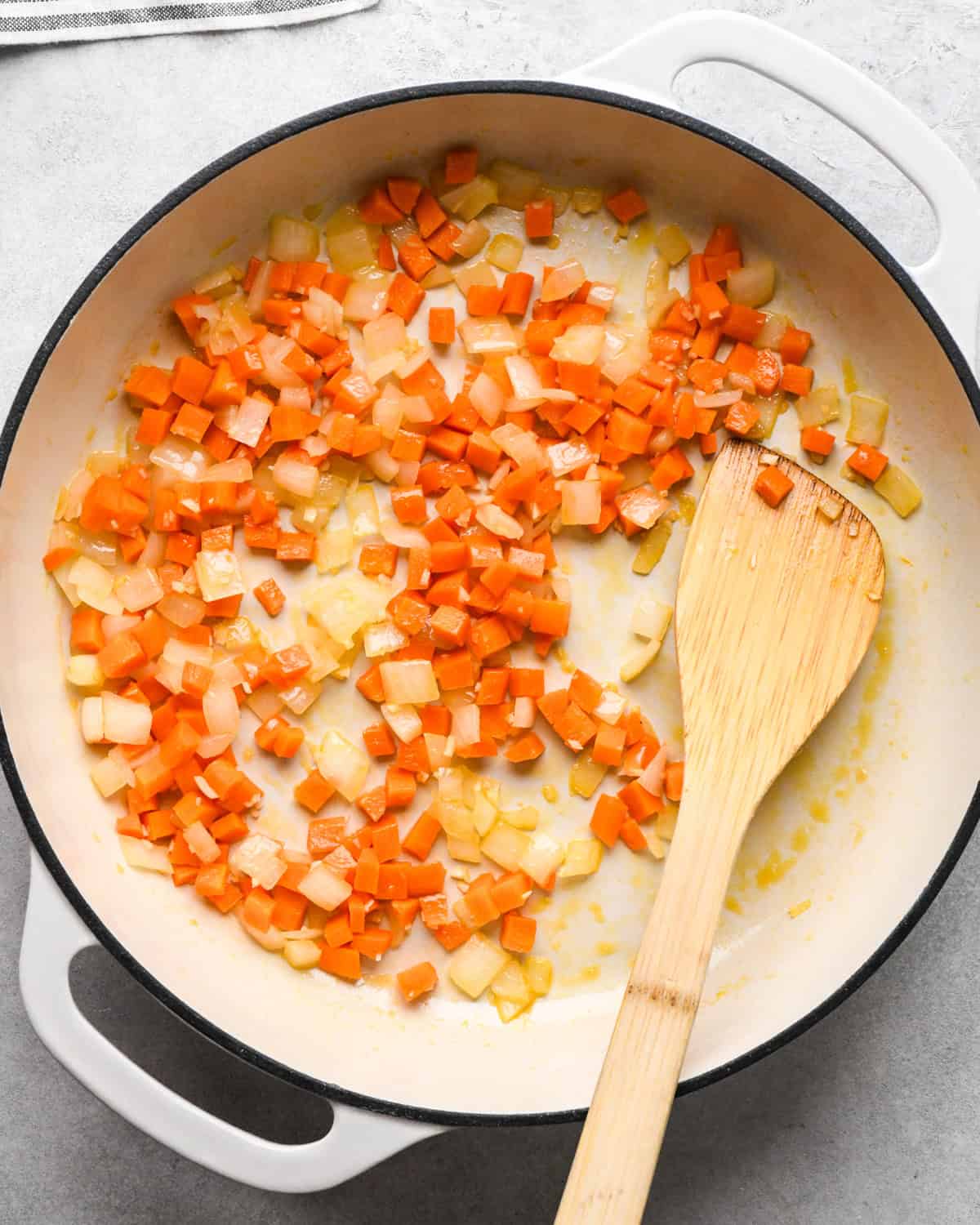 Making chicken fried rice: overhead photo of vegetables being sautéed in a white skillet with a wooden spatula.