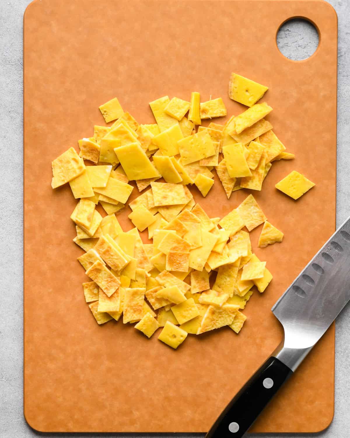 Making chicken fried rice: overhead photo of cooked eggs on an orange cutting board being chopped up with a knife.