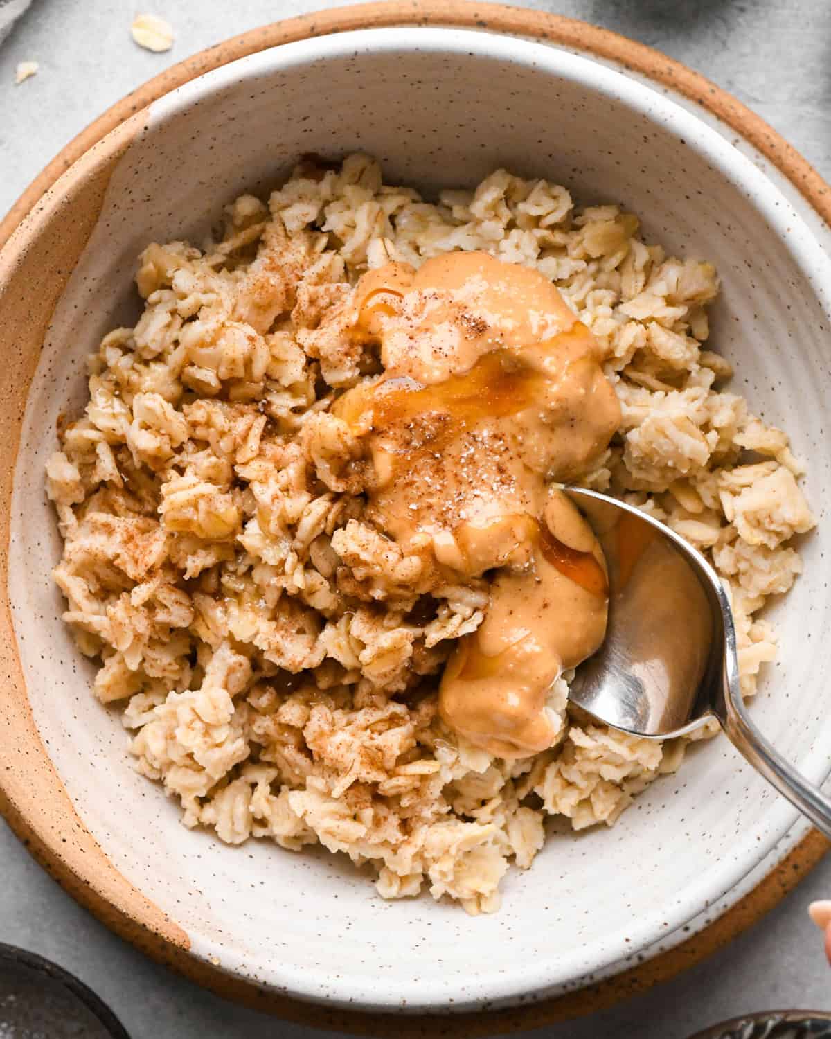a bowl of cooked oatmeal with peanut butter and honey on top with a silver spoon taking a scoop