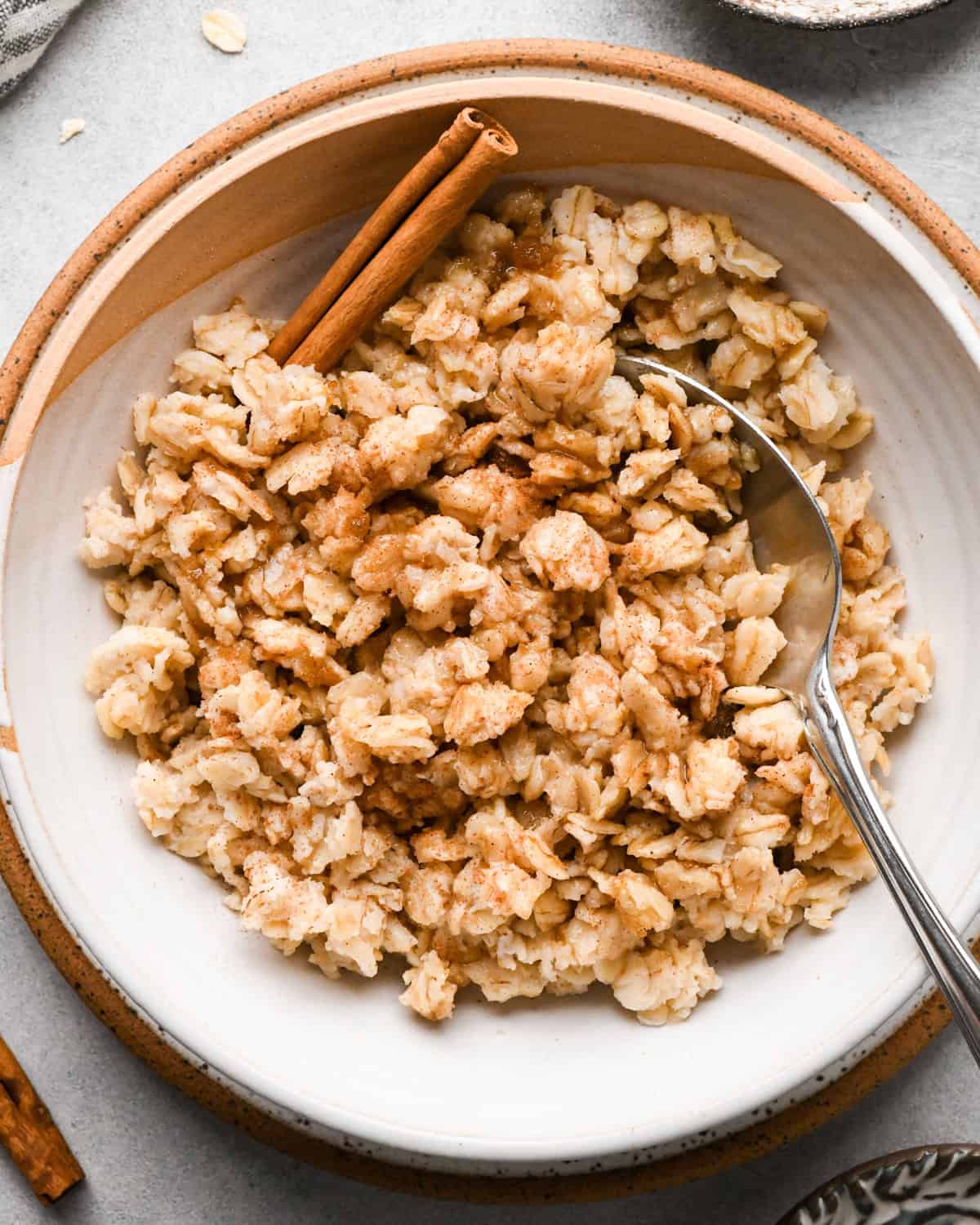 oatmeal in a bowl with, cinnamon and a cinnamon stick. A hand is holding a silver spoon taking a bite.