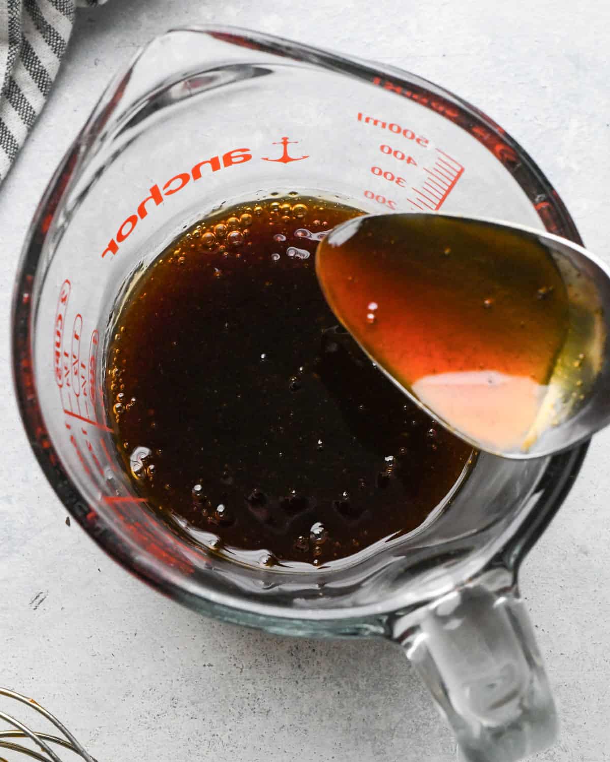 Making teriyaki chicken: close-up photo of teriyaki sauce in a clear glass measuring cup being served with a spoon.