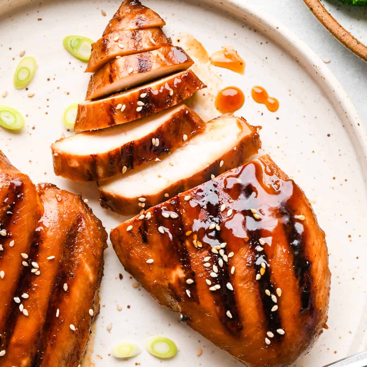A plate of sliced homemade teriyaki chicken topped with sesame seeds and green onions.