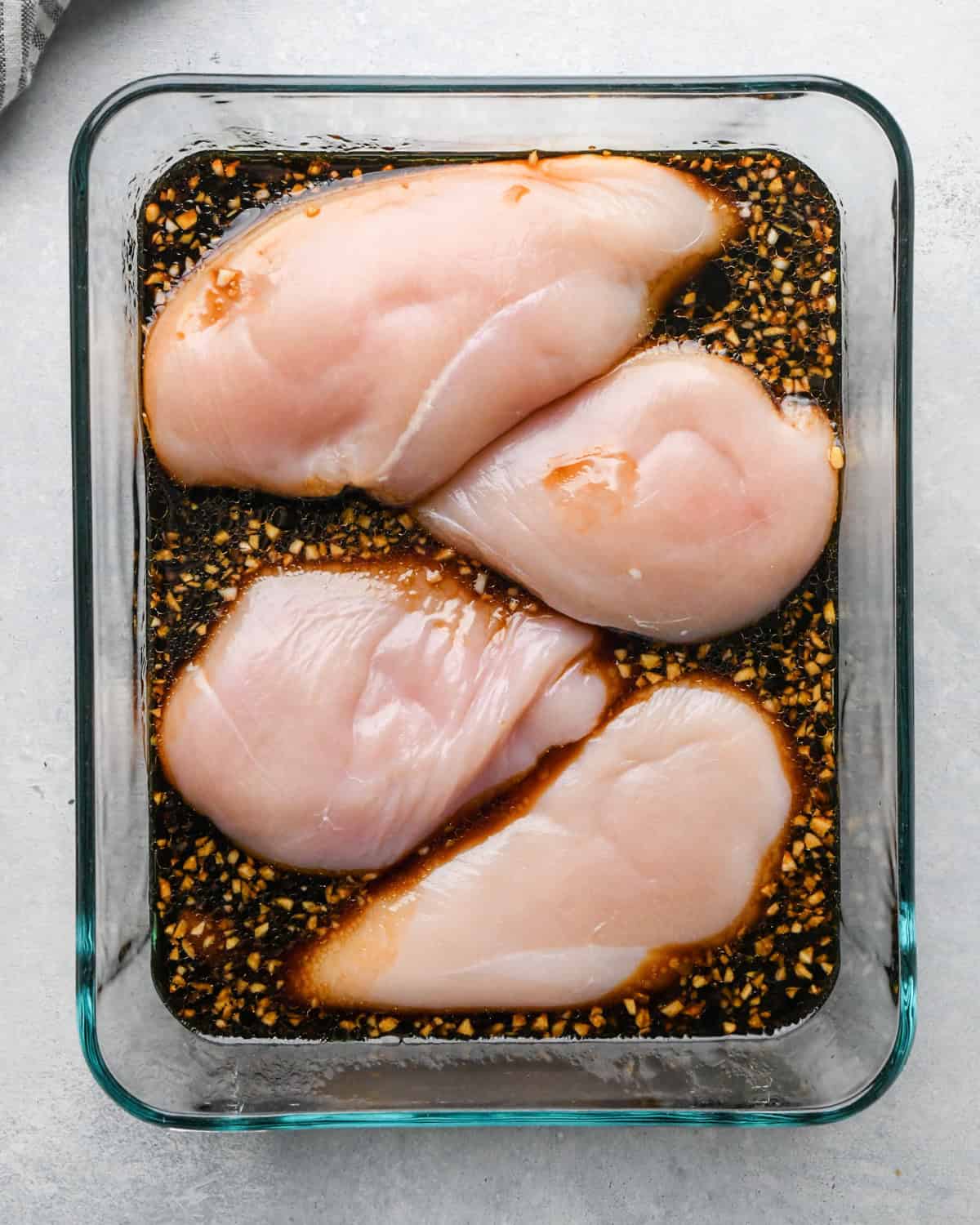 Making teriyaki chicken: overhead photo of chicken breasts and teriyaki sauce placed together in a clear rectangle Pyrex dish.