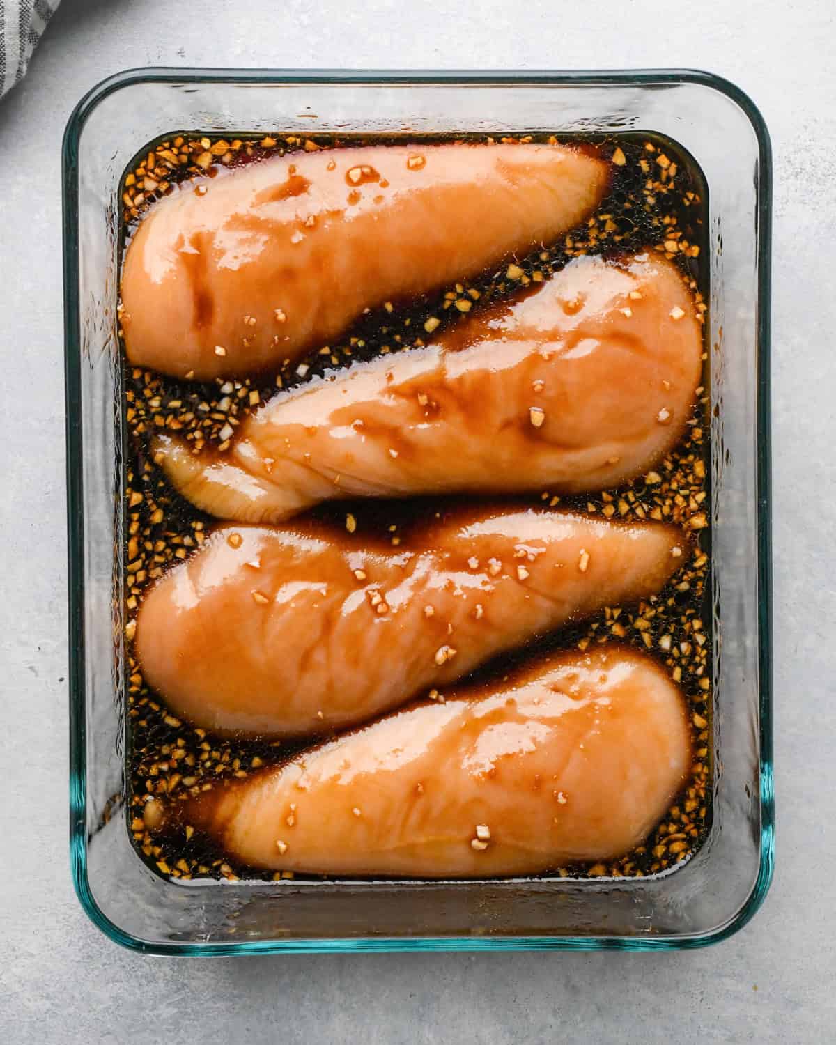 Making teriyaki chicken: overhead photo of chicken breasts and teriyaki sauce placed together in a clear rectangle Pyrex dish.