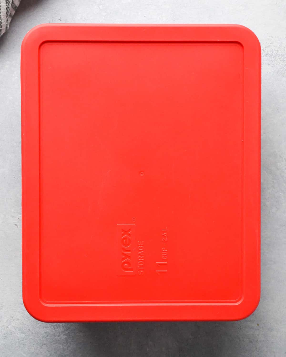 Making teriyaki chicken: overhead photo of chicken breasts and teriyaki sauce placed together in a clear rectangle Pyrex dish and covered with a red lid for marinating.