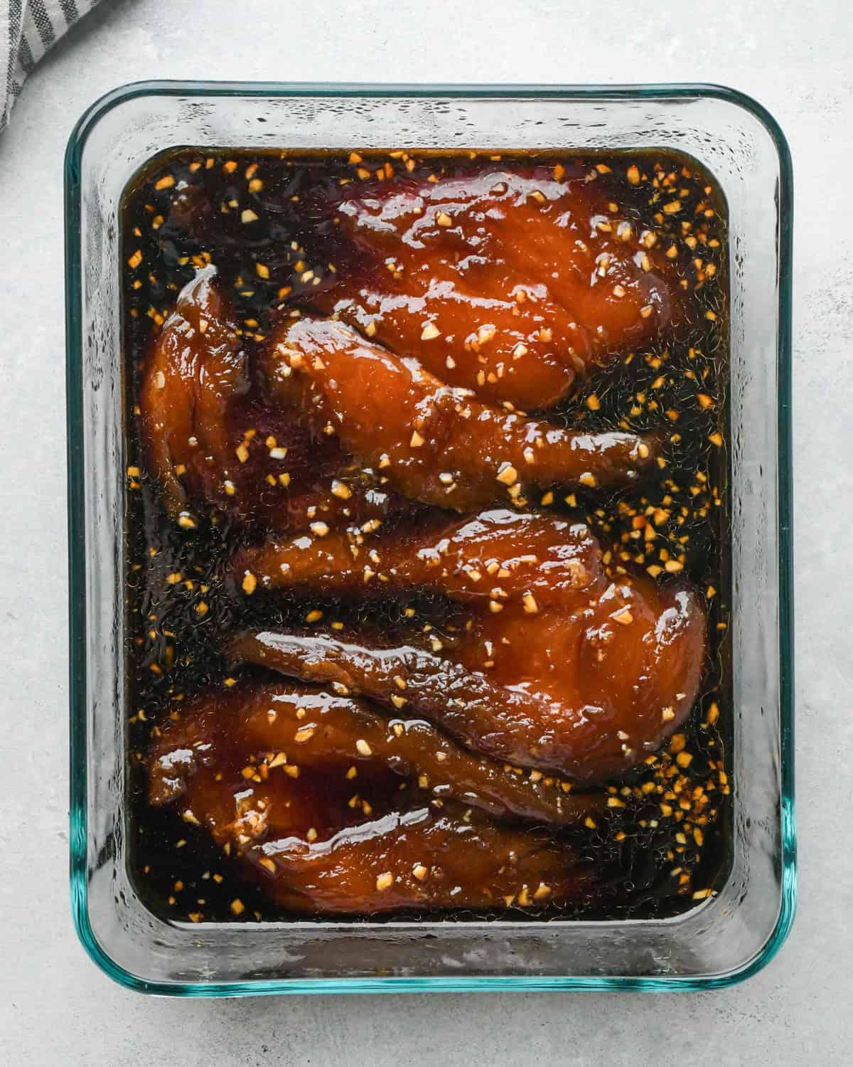 Making teriyaki chicken: overhead photo of chicken breasts marinated in teriyaki sauce in a clear rectangle Pyrex dish.