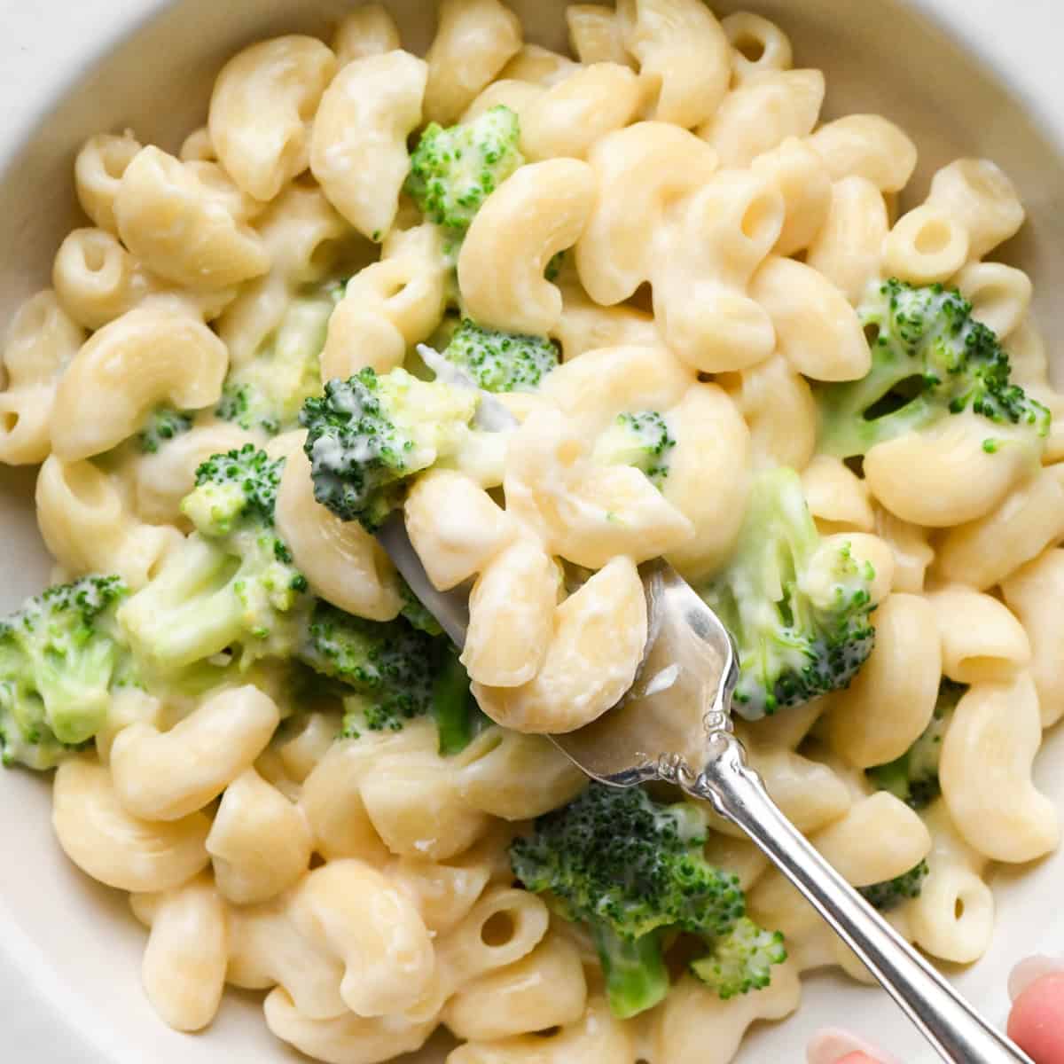 Close-up photo of creamy broccoli mac and cheese in a white bowl, made with elbow pasta and tender broccoli florets and coated in homemade cheese sauce and being served with a fork.