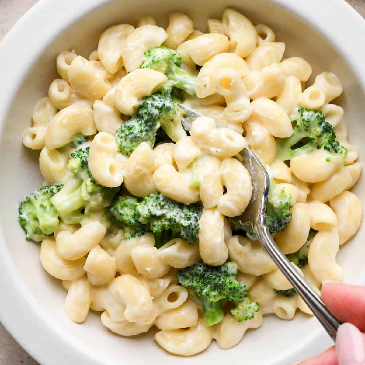 Close-up photo of creamy broccoli mac and cheese in a white bowl, made with elbow pasta and tender broccoli florets and coated in homemade cheese sauce. Being served with a fork.