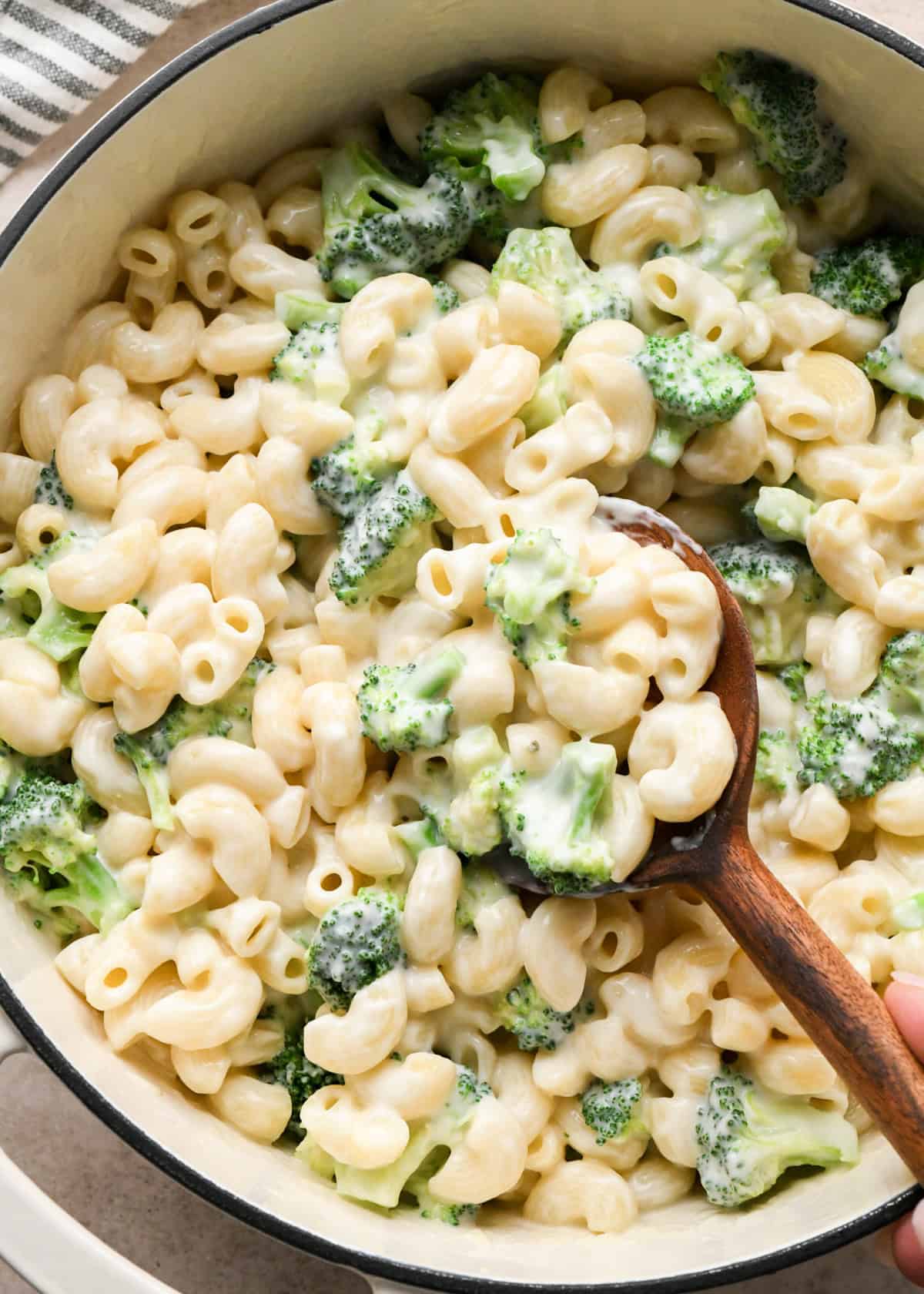 Close-up photo of creamy broccoli mac and cheese with elbow pasta coated in homemade cheese sauce and tender broccoli florets, being stirred with a wooden spoon.