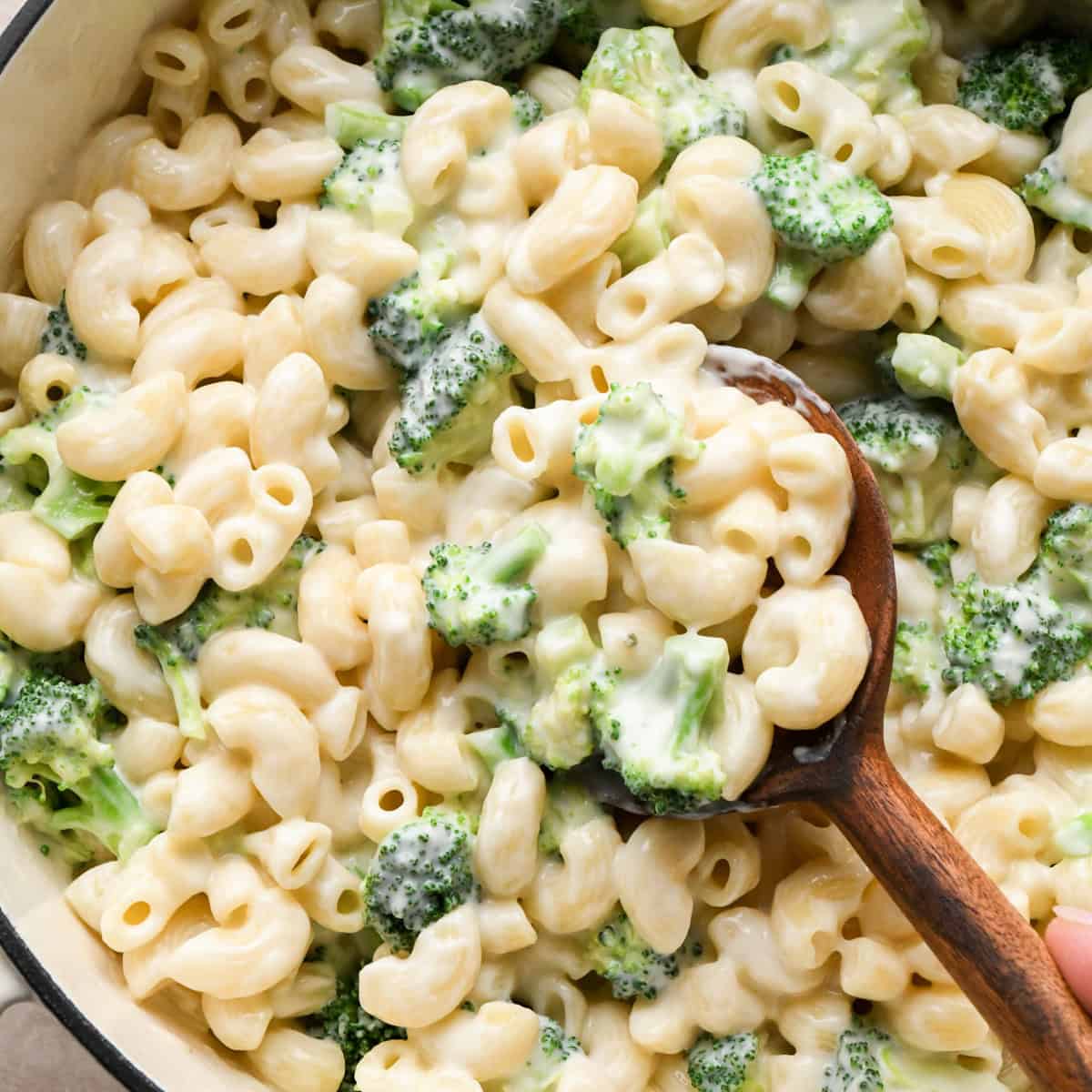 Close-up photo of creamy broccoli mac and cheese with elbow pasta coated in homemade cheese sauce and tender broccoli florets, being stirred with a wooden spoon.