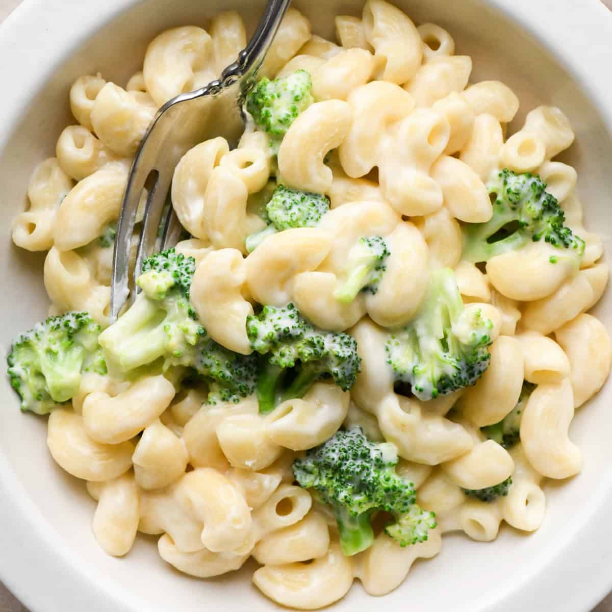 Close-up photo of creamy broccoli mac and cheese in a white bowl, made with elbow pasta and tender broccoli florets and coated in homemade cheese sauce and being served with a fork.