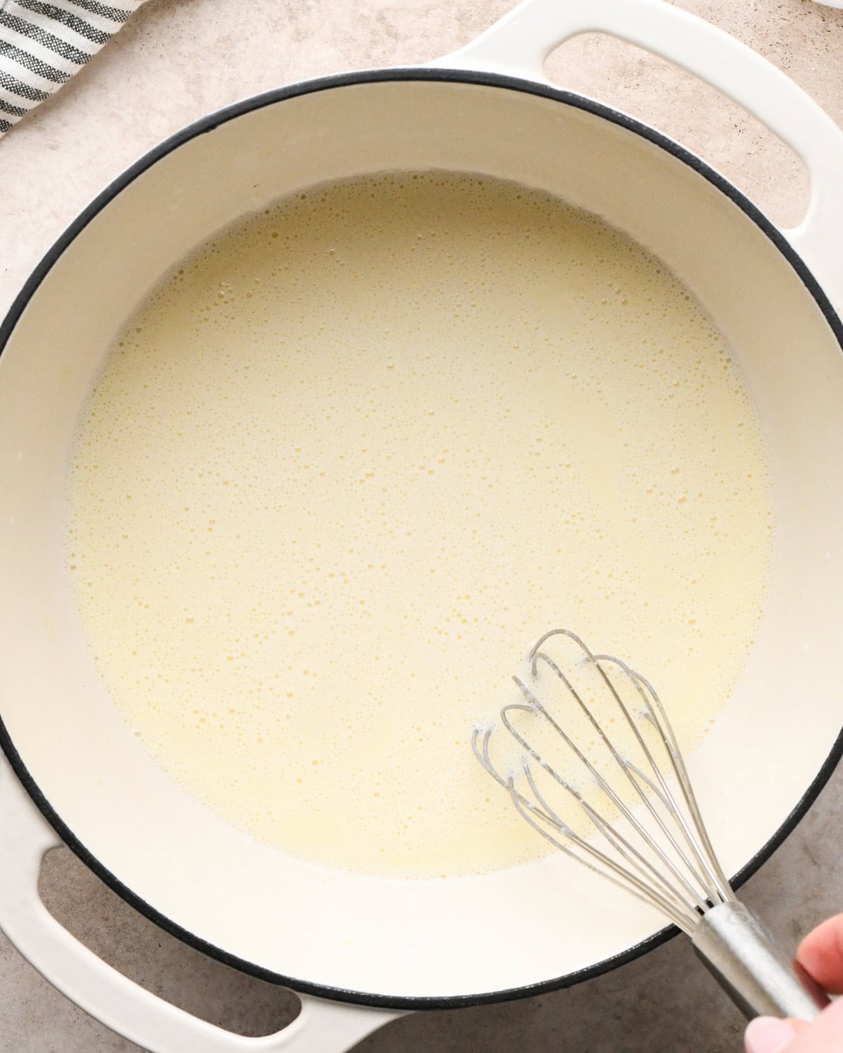Making broccoli macaroni and cheese (mac and cheese): overhead photo of milk being added to simmering homemade cheese sauce in a large pot and whisked together.