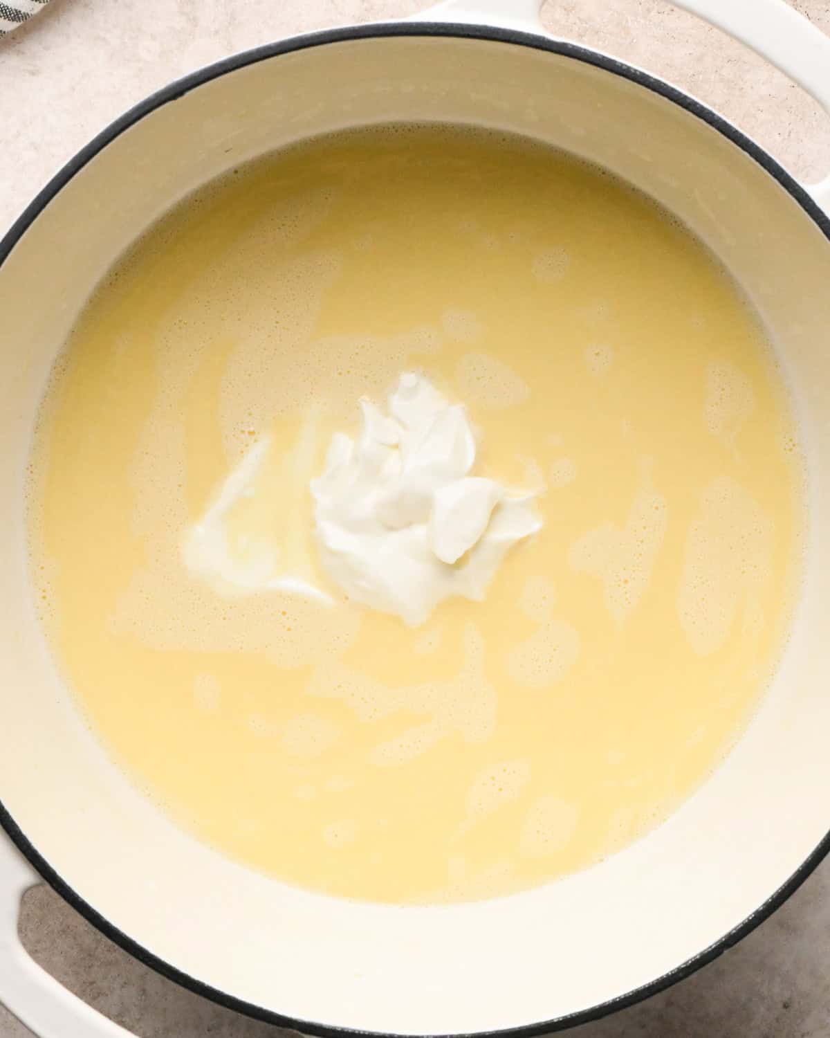 Making broccoli macaroni and cheese (mac and cheese): overhead photo of sour cream being added to homemade cheese sauce in a large pot.