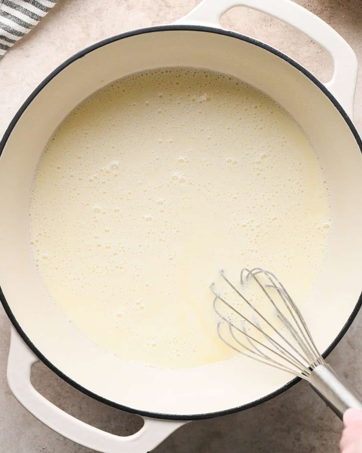 Making broccoli macaroni and cheese (mac and cheese): overhead photo of sour cream being added to homemade cheese sauce in a large pot and whisked together.